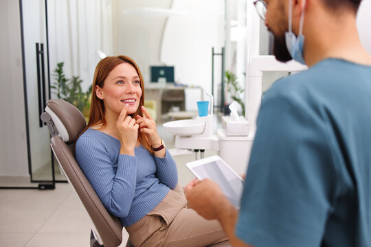 Patient in dental chair consults with dentist, pointing to teeth and smiling during a friendly checkup in a modern clinic focused on oral health and confident smiles