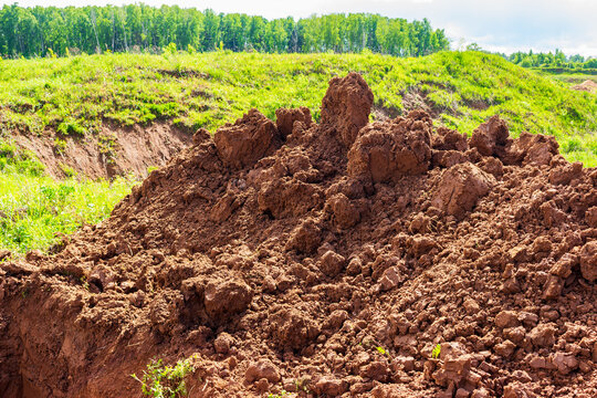 Large pile of freshly excavated raw clay soil on a green meadow, dug up by heavy construction machinery during site development, textured dirt mounds in rural countryside area