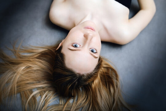 Young woman lying upside down with flowing hair and direct gaze.