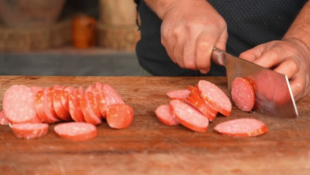 Chef slicing cured salami sausage on wooden cutting board