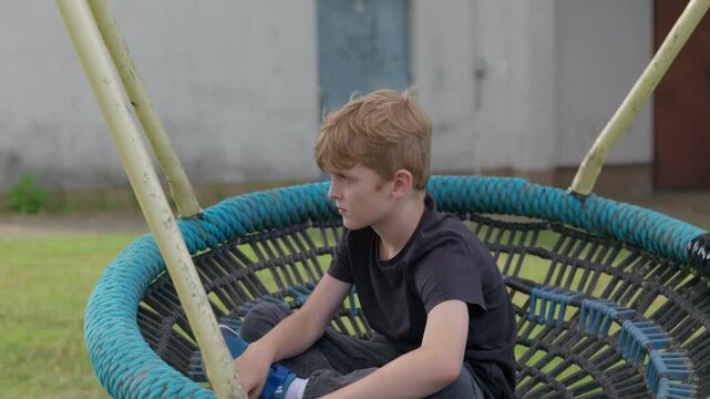 A serious boy is swinging on a swing slow motion focus transition from blur to sharpness