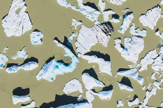 Aerial view of icebergs floating in the glacial lagoon of Fjallsarlon, with white ice fragments contrasting against the murky water in Sveitarfelagid Hornafjordur, Iceland.