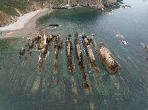 Aerial view of the unique flysch rock formations protruding from the clear coastal waters with a sandy beach in the background in Spain.