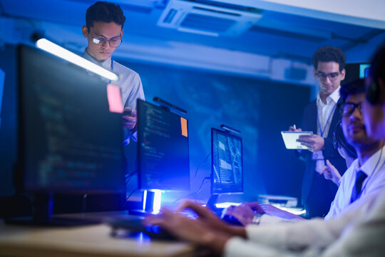 A night-shift analyst reads through a stack trace on screen with one hand on the keyboard and the other raised toward the screen inside a modern technology office at night