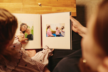 Caucasian mother and child browsing printed family photo album together indoors. Suitable for...