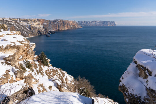 Snowy limestone cliffs overlook the deep blue Black Sea under a clear winter sky on a cold sunny day