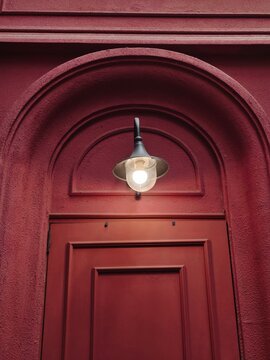 Glowing vintage style sconce wall lamp mounted above arched red door frame.