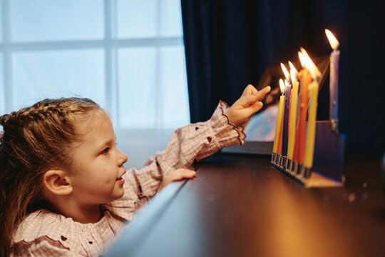 Caucasian child pointing at burning Hanukkah menorah candles at home. Jewish holiday celebration concept for cultural storytelling, religious education, and festive seasonal marketing