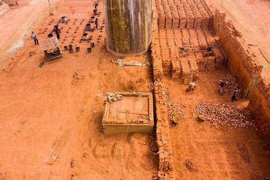 Aerial view of the brick kiln in Aminbazar with workers stacking bricks near a large chimney and piles of clay on the red earth ground in Aminbazar, Dhaka Division, Bangladesh.