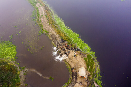 Aerial view of water pumps discharging into the river near a small shelter on the riverbank with green vegetation in Aminbazar, Dhaka Division, Bangladesh.