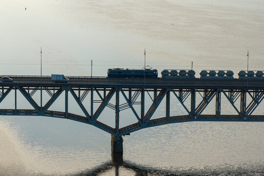 Aerial view of a cargo train and vehicles crossing a steel truss bridge over a calm river in Poland.