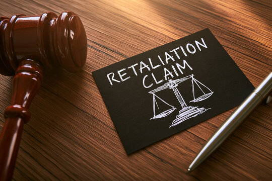 A wooden gavel and a card with the text Retaliation Claim lie on a desk in bright lighting.