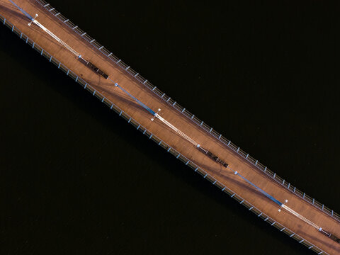 Aerial view of a wooden pier on the river with metal railings and lighting fixtures stretching across dark water in Poland.