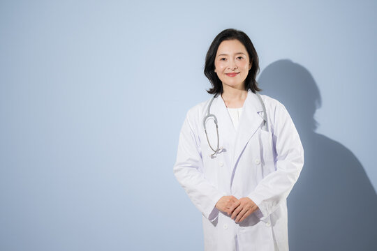 [Light blue background] A female doctor wearing a stethoscope and a white coat, smiling and looking directly at the camera&mdash;a portrait of a Japanese doctor