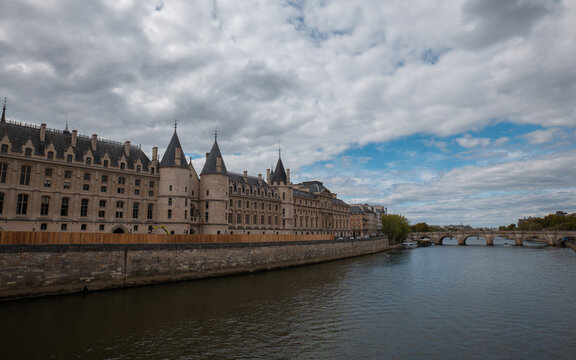 Conciergerie palace and seine river flowing past pont neuf bridge under cloudy sky in paris, france