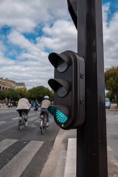 Green traffic light giving right of way to cyclists riding on a paris city street under a cloudy sky