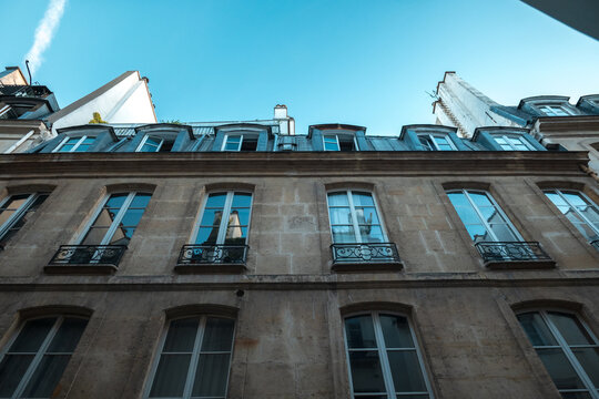 Parisian haussmann building facade with windows and classic wrought iron balconies against blue sky