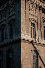 Obraz premium Louvre museum facade in paris, france, showing architectural detail, columns, and windows with sunlight and shadow