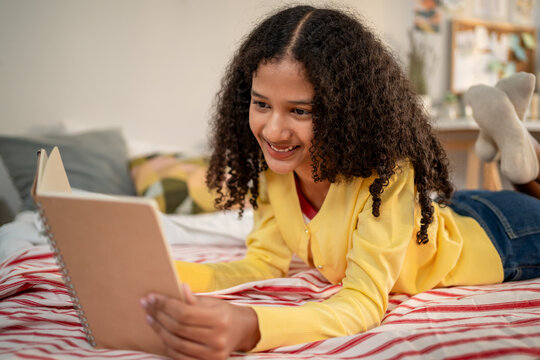 African American teenage girl lying on comfort bed and reading a book. 