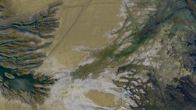 Aerial view of the intricate tidal channels and mudflats of Khor Al Zubair with patches of green vegetation in the arid landscape of Khor Al Zubair, Basra Governorate, Iraq.