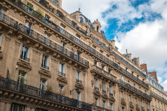 Haussmann style building facade with ornate wrought iron balconies and blue sky in paris, france