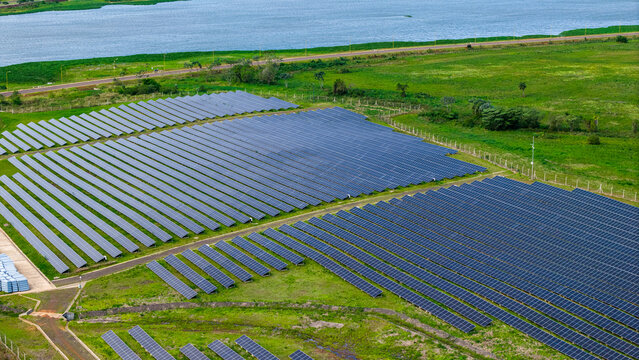 Aerial view of a large solar farm with rows of photovoltaic panels set in a green landscape near a river in Posadas, Misiones Province, Argentina.