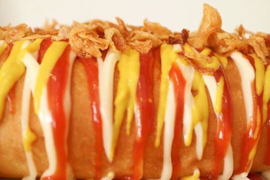 Front view of a delicious hotdog topped with fried onions and artistic drizzled sauces