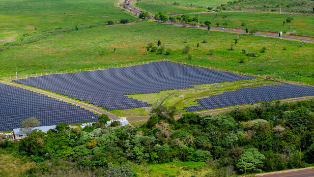 Aerial view of a large solar farm with rows of photovoltaic panels set in a green landscape near a road in Posadas, Misiones Province, Argentina.