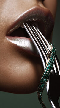 Close up of metallic silver lips and reflective fork with emerald rings in still life