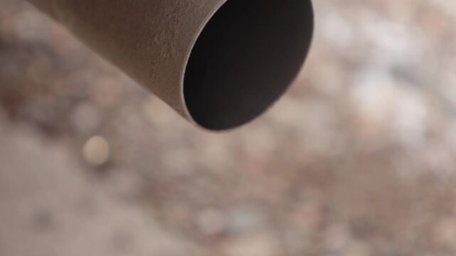 Circular car exhaust pipe emitting a faint trace of smoke with a blurred background, showcasing the metallic tubing and emphasizing automotive emission components.