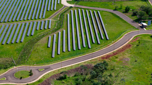 Aerial view of solar panels for renewable energy arranged in rows across a green landscape with a nearby road and roundabout in Posadas, Misiones Province, Argentina.