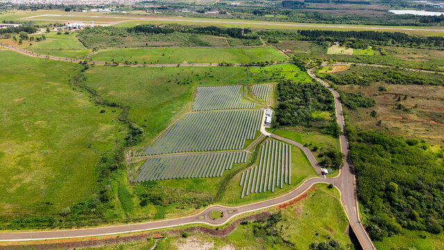 Aerial view of a solar farm with rows of photovoltaic panels set in a green landscape near a road and airport runway in Posadas, Misiones Province, Argentina.