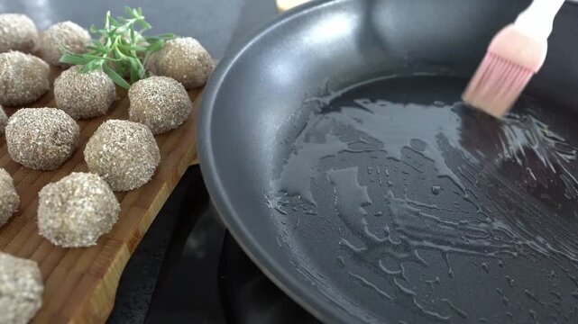 A woman brushes oil onto a frying pan before cooking. Concept: moderate fat consumption.