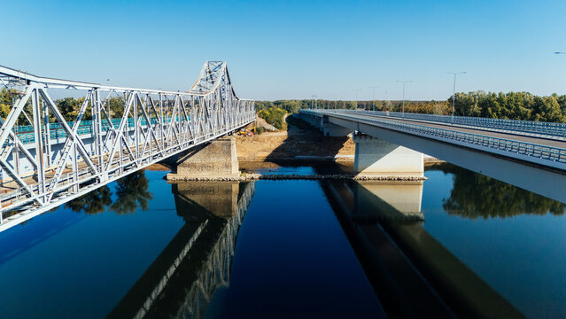 Aerial view of the Racha Bridge spanning the Sava River with its steel truss structure alongside a modern concrete bridge under a clear blue sky in Sremska Raca, Vojvodina, Serbia.