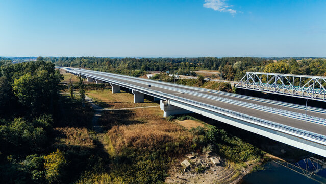 Aerial view of the Racha Bridge highway infrastructure spanning the river with an adjacent historic truss bridge, surrounded by forest under a clear sky in Sremska Raca, Vojvodina, Serbia.
