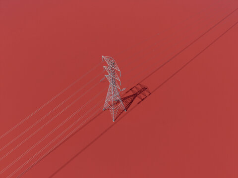 Aerial view of San Francisco Bay Salt Ponds featuring a high-voltage electricity pylon casting a long shadow over the vibrant red water in Fremont, California, United States.