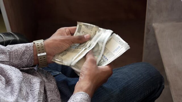 Person sitting and counting Indian rupee currency notes cash money