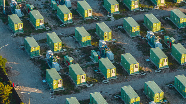 Aerial view of modular battery storage containers and electrical transformers arranged in a grid pattern at an energy storage facility in Trino, Piedmont, Italy.