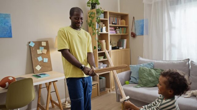 African American father playing wooden toy sword fight with child son in slow motion at home. Footage representing family bonding suitable for parenting commercials and lifestyle marketing