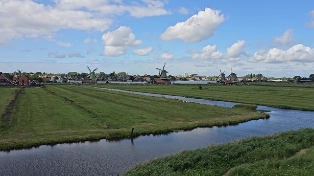 Static horizontal wide view of polder canals and traditional windmills in Zaanse Schans, Netherlands.