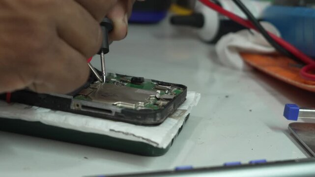 Technician testing smartphone motherboard circuit board with multimeter probes