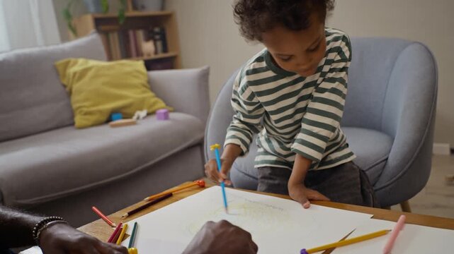 African American father watching young son drawing with colored pencils on paper at home table. Footage suitable for parenting commercials and early childhood education marketing
