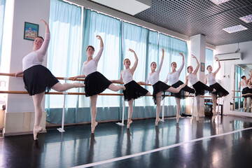 Female ballet dancers practicing barre exercises in bright studio light © TRAVELARIUM