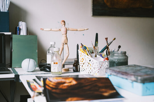 A wooden drawing mannequin and art supplies sit on a desk in a creative art studio. Authentic local small business concept for inspiring art classes.