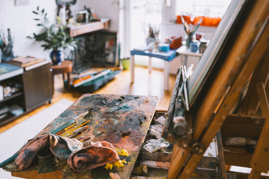 A wooden palette with mixed colorful oil paints rests on an easel in an art studio. Authentic local small business concept for painting art classes.