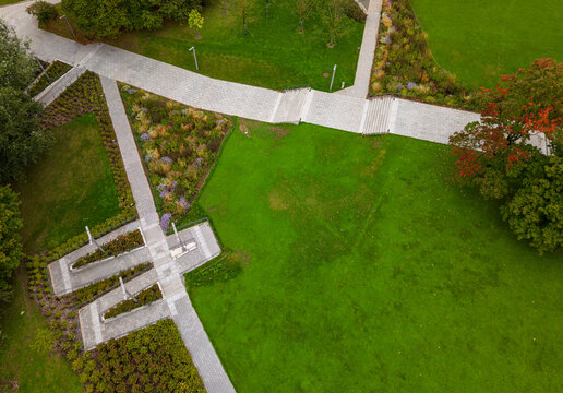 Aerial view of a public park featuring paved walkways, manicured green lawns, flower beds, and trees with early autumn foliage in Vilnius, Vilnius County, Lithuania.