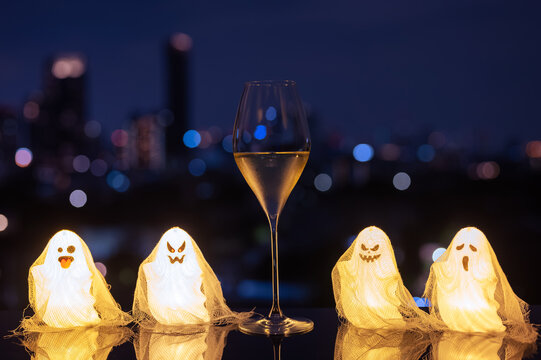 Halloween white wine glass flanked by glowing ghost lights against a city skyline at night.