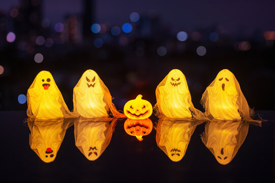 Halloween glowing ghosts with a small pumpkin and reflections against a city skyline at night.
