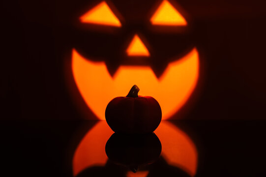 Halloween pumpkin silhouette against a glowing jack o lantern face and reflection.