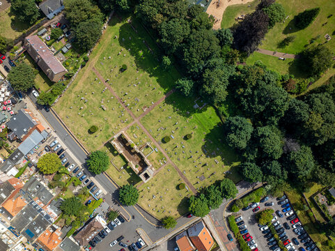 Aerial view of the ruins of St Andrew's Old Kirk in a historic graveyard with mature trees, adjacent to streets and parking in North Berwick, Scotland, United Kingdom.